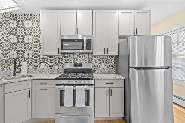 Modern kitchen with light gray cabinets, stainless steel appliances, and patterned backsplash.