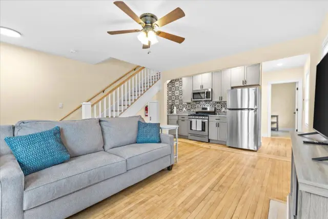 Living room with gray sofa, kitchen, stairs, and hardwood floors.