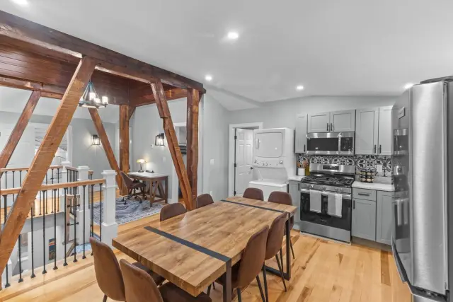 Open-concept living space with kitchen, dining area, and living room. Exposed wooden beams, wood floors, and neutral walls.