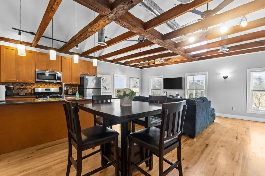 Renovated apartment with exposed wood beams, hardwood floors, stainless steel appliances and an open kitchen and living area.